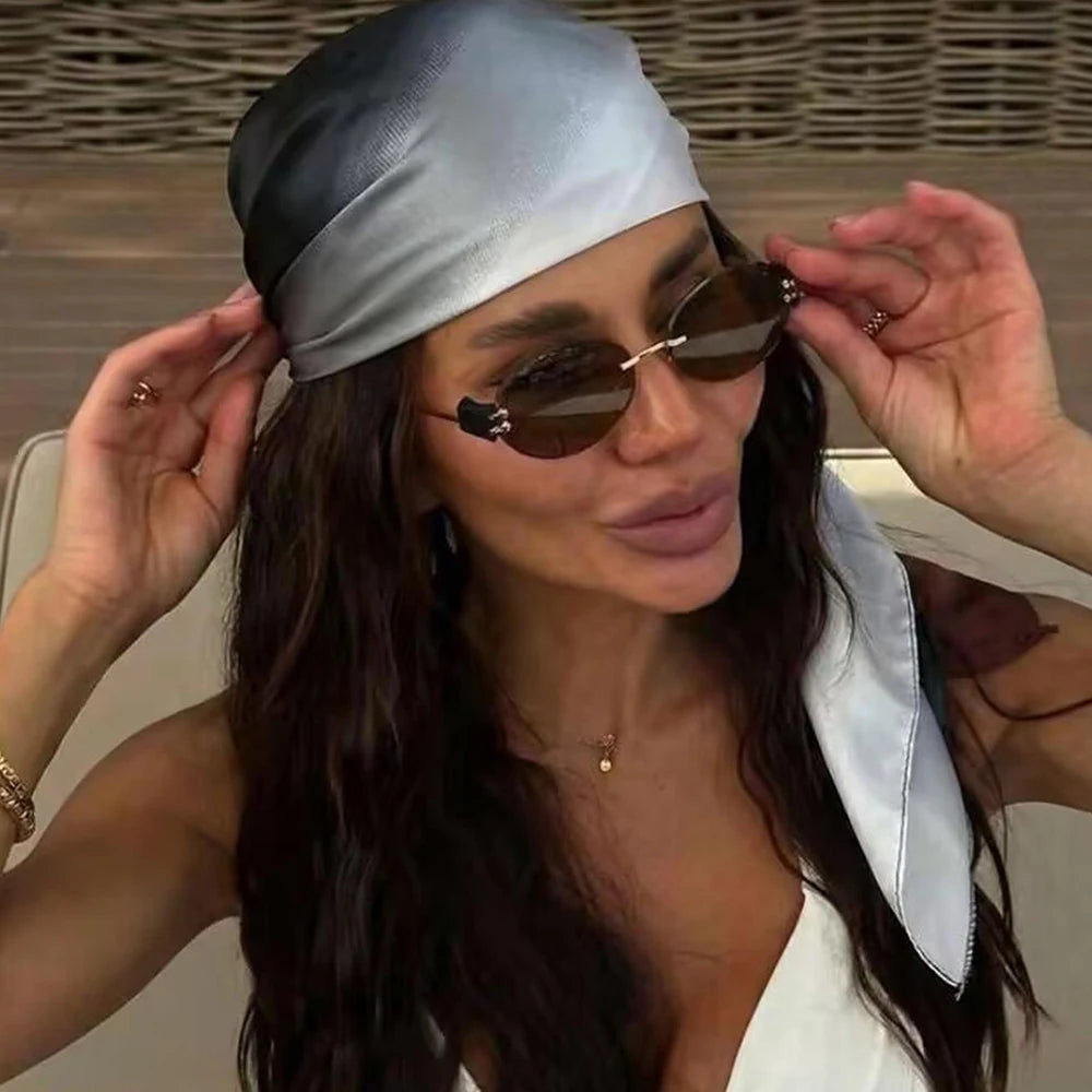 Une femme portant un hijab à dégradé argenté et des lunettes de soleil, tenant le tissu sur sa tête.