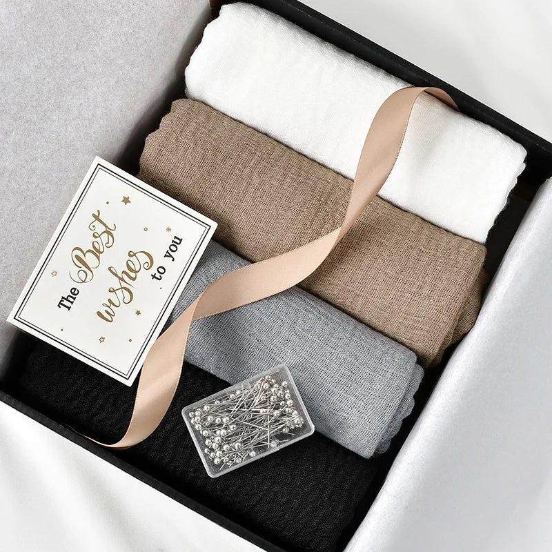 Une boîte contenant un ensemble de foulards hijab en mousseline de coton élégants, avec des pièces de tissu beige et blanc.