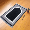 Una elegante alfombra de oración en blanco y negro con borde y flecos decorativos sobre un suelo de madera.