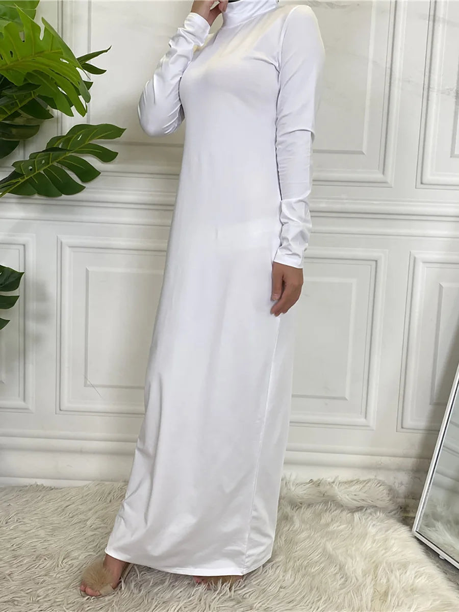 Langes weißes, elegantes Abaya-Kleid mit langen Ärmeln und hohem Ausschnitt vor einer weißen Wand