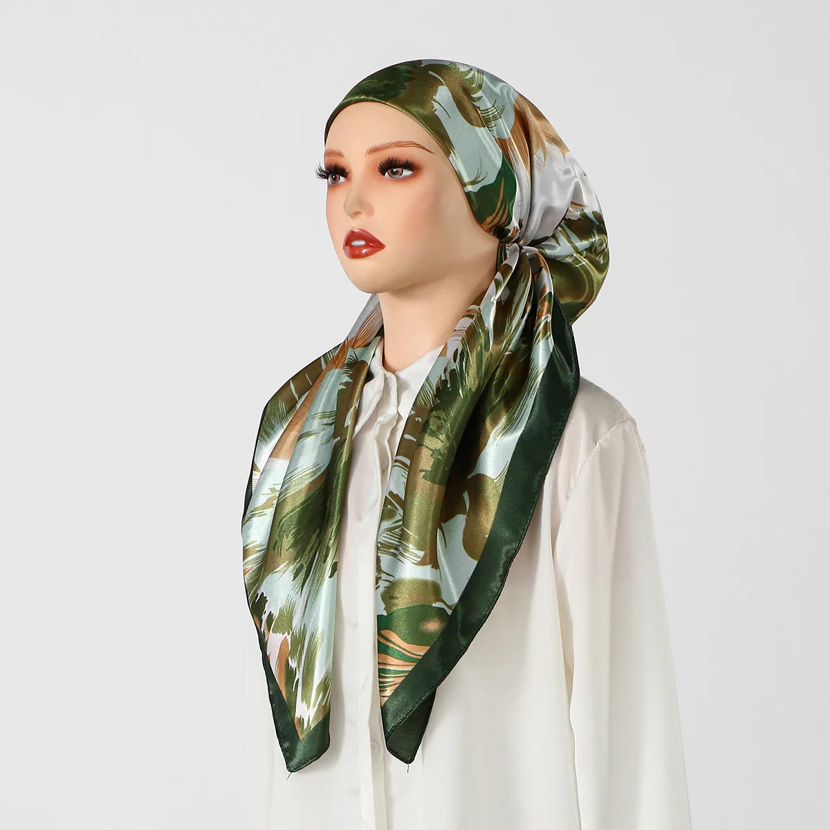 Eine Frau trägt einen satinbedruckten grünen und beigen tropischen Blätter-Hijabschal um ihren Kopf.