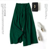 Dunkelgrüne Leinenmischhose mit weit geschnittenen Palazzo-Beinen neben einer schwarzen Clutch und weißen bestickten Schuhen.