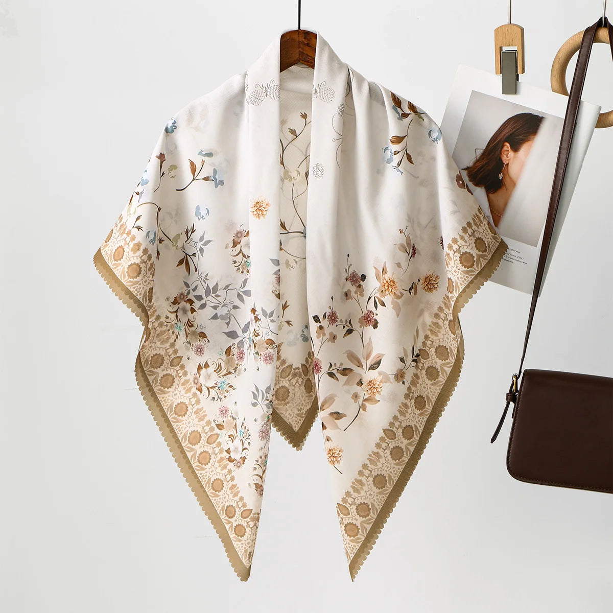 Cremiges Blumen-Karo-Hijabschal mit zarten Aquarell-Botanikal-Prints und Goldrand, aufgehängt an einem Holzbügel.