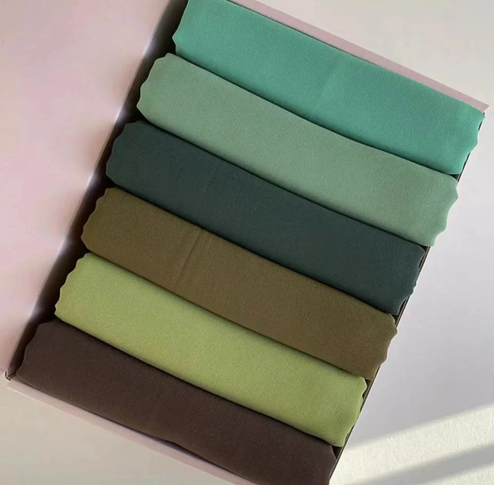 Ein Set von sechs pastellfarbenen Chiffon-Hijabs in verschiedenen Grüntönen und Olivfarbe, ausgelegt in einer Box.
