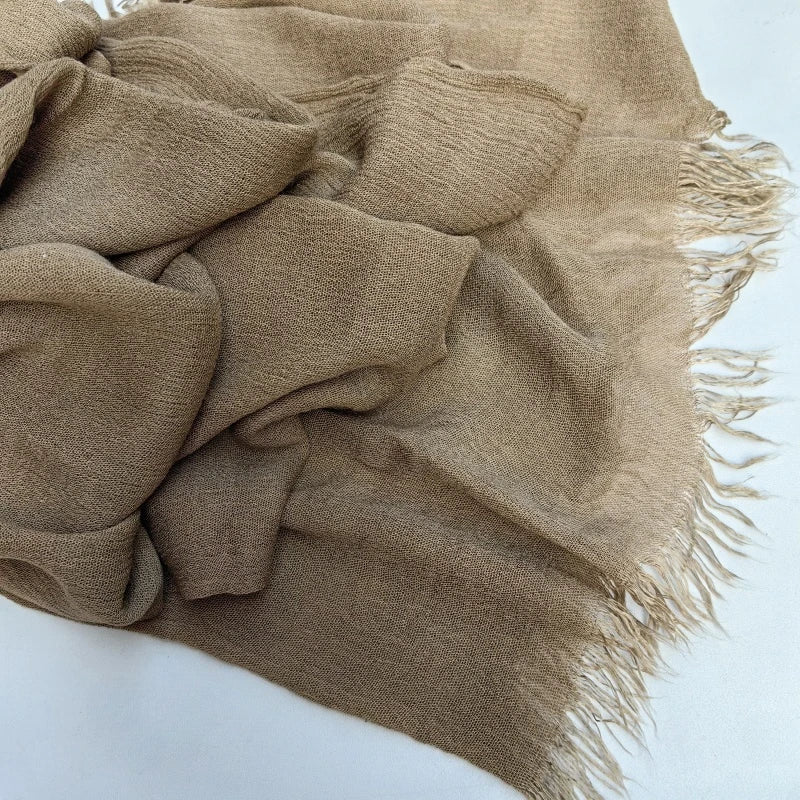 Écharpe hijab en coton viscose beige avec franges et pompon, drapée sur une surface blanche.
