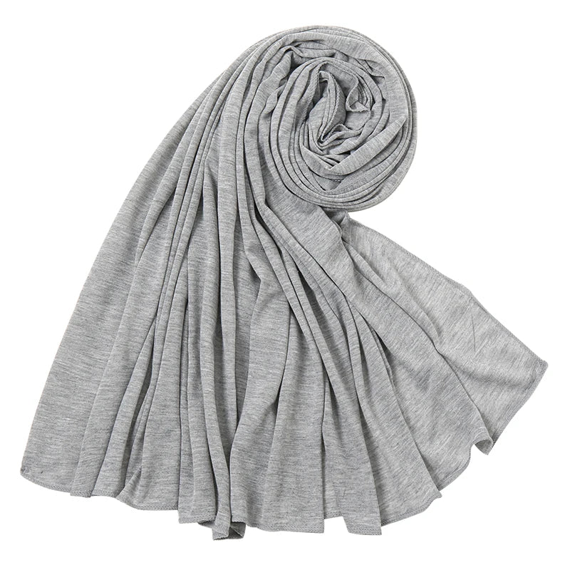 Ein grauer Baumwoll-Jersey-Hijab-Schal ist gerollt und drapiert, zeigt seine weiche Textur.