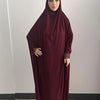 Une femme portant une caftan abaya fluide bordeaux avec un hijab, debout sur un fond clair.