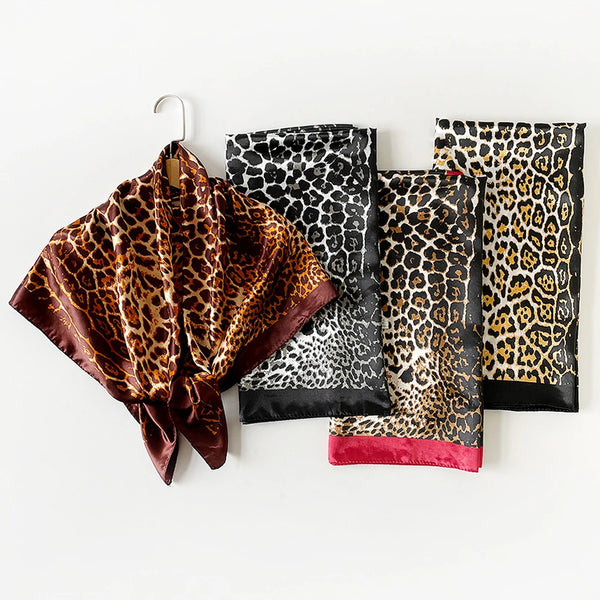 A stack of leopard print silk square scarves in black, gold, and brown tones displayed on a hanger.