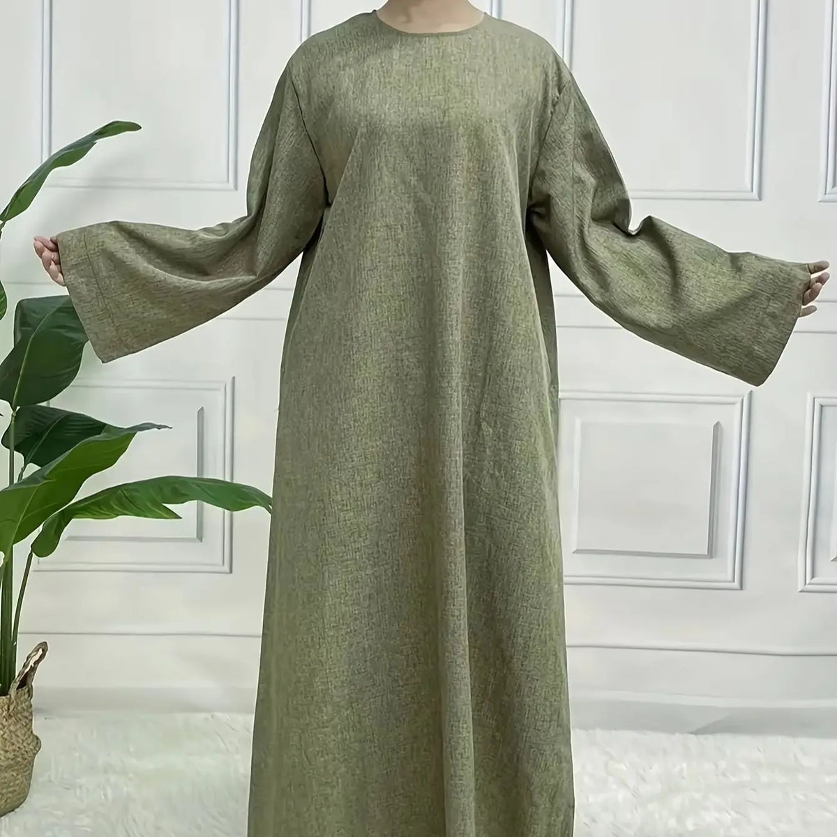 Vestido kaftan verde oliva de largo completo con mangas largas, exhibido contra una pared de paneles blancos.