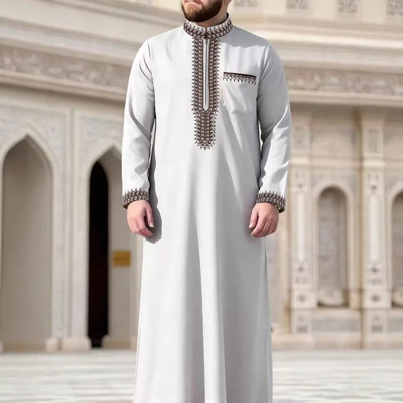 Un hombre vistiendo una jubba thobe casual de color gris claro bordada en un entorno arquitectónico ornamentado.