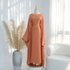 Terrakotta-orange Kaftan-Kleid mit Schmetterlingsärmeln auf einem Mannequin neben einer Topfpflanze.