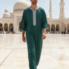 Mann in eleganter smaragdgrüner bestickter muslimischer Robe in einem Hof mit Moscheearchitektur