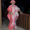 A woman models an elegant flowing pink kaftan with white tatting detail in an outdoor setting.