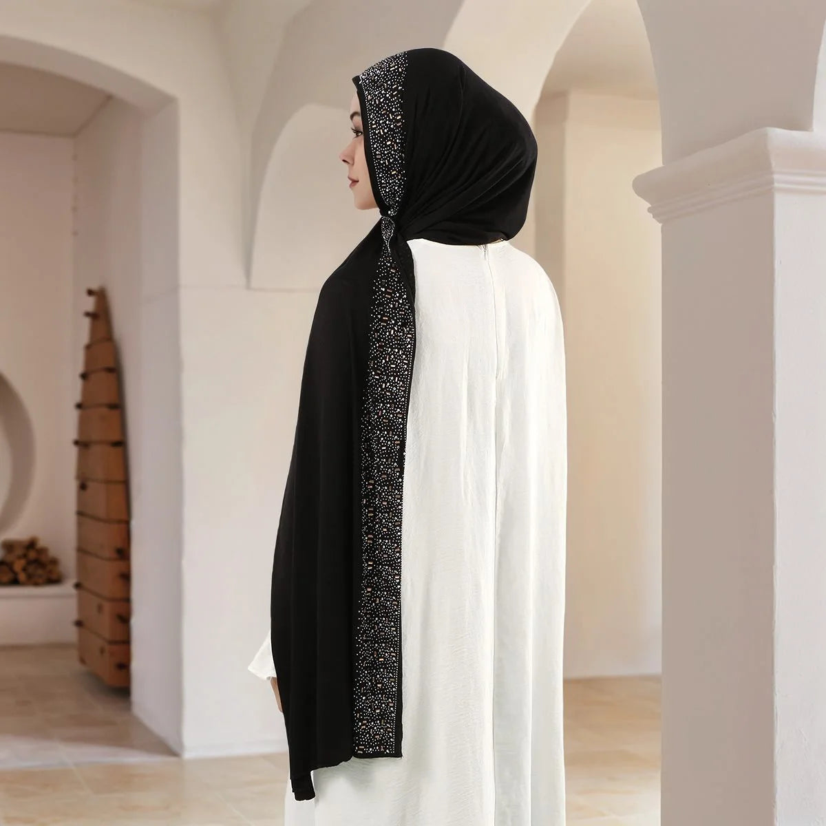 Eine Frau mit schwarzem Diamant-Schal und weißem Kleid steht in einem Gewölbten Gang.