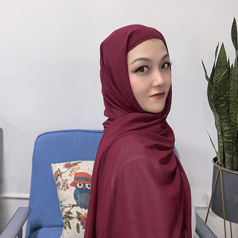 Una mujer vistiendo un conjunto de hijab y chal de chiffon instantáneo color granate, mirando a la cámara.