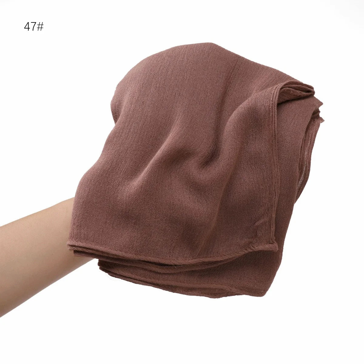 Écharpe châle en rayon froissé de couleur rose poudré, pliée et poussiéreuse, tenue par une main.