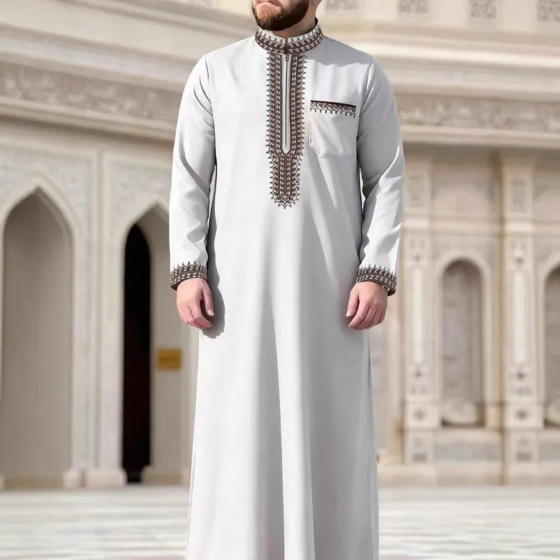 Un hombre vistiendo una jubba thobe bordada de gris claro en un entorno arquitectónico ornamentado.