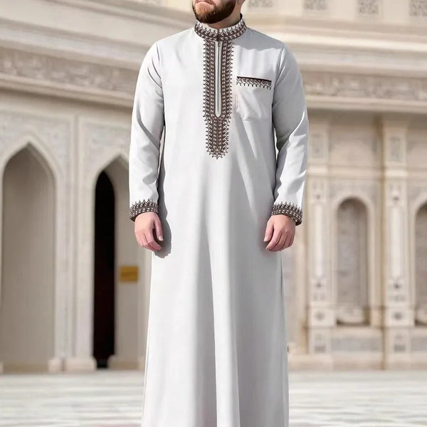 A man wearing a light gray embroidered jubba thobe casual robe in an ornate architectural setting.