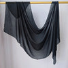 Foulard hijab noir uni drapé sur un cintre en bois sur fond blanc.