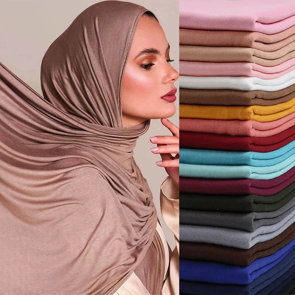 A close-up of a woman wearing a brown modal jersey hijab scarf next to a stack of various colored fabric rolls.