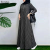 Eine Frau in einem schwarz-weißen gestreiften Maxi-Kleid und schwarzem Hijab vor einer weißen Wand.
