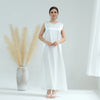 A woman models a white flowing modest abaya dress with a simple neckline against a light background.