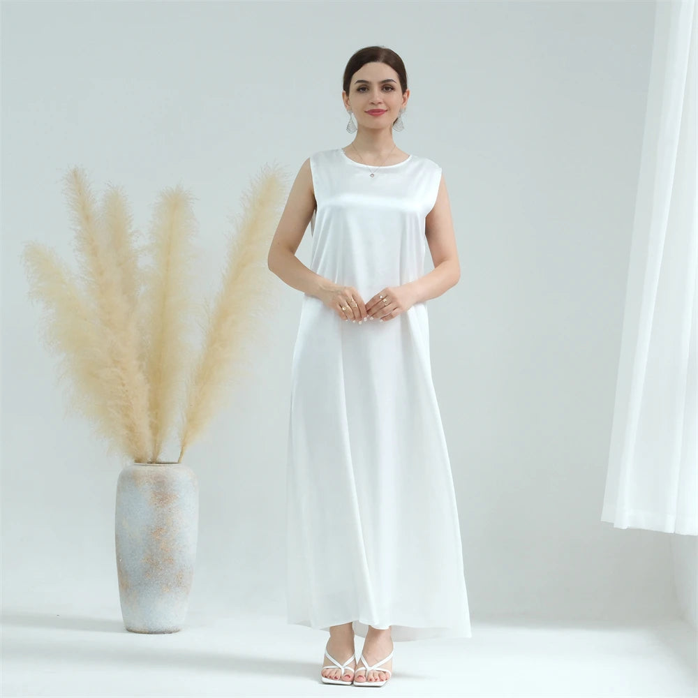 A woman models a white flowing modest abaya dress with a simple neckline against a light background.