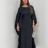 Una mujer modela un vestido abaya de satén negro tipo batwing con mangas largas y una falda fluida.