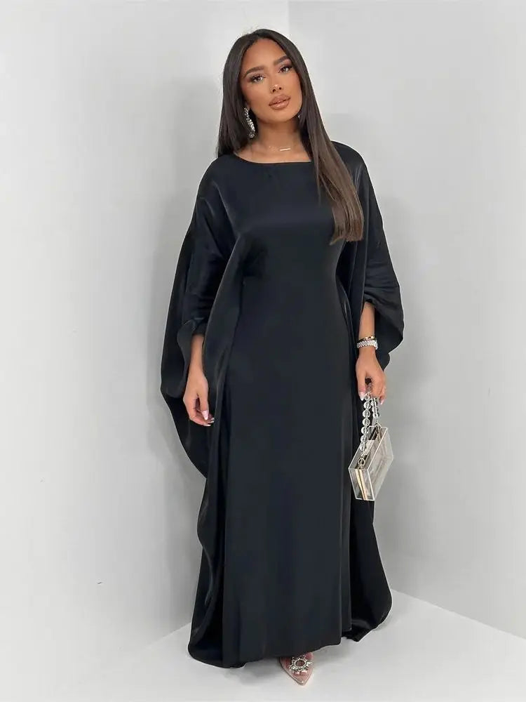 Una mujer modela un vestido abaya de satén negro tipo batwing con mangas largas y una falda fluida.