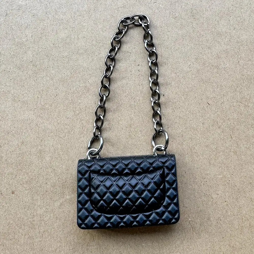 Bolso de cuero acolchado negro con correa de cadena plateada sobre fondo marrón neutro.