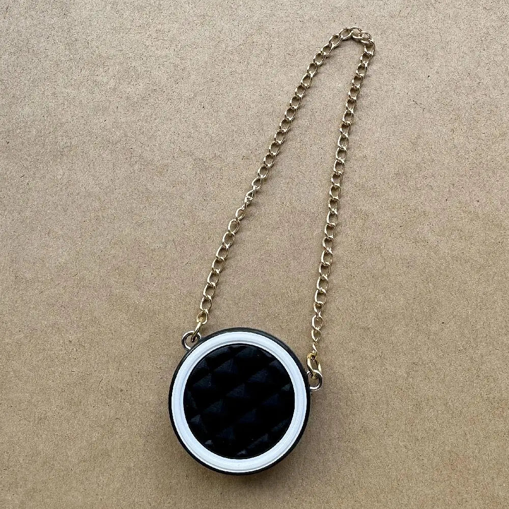 Collar de cadena dorada con colgante de patrón blanco y negro redondo sobre papel marrón.