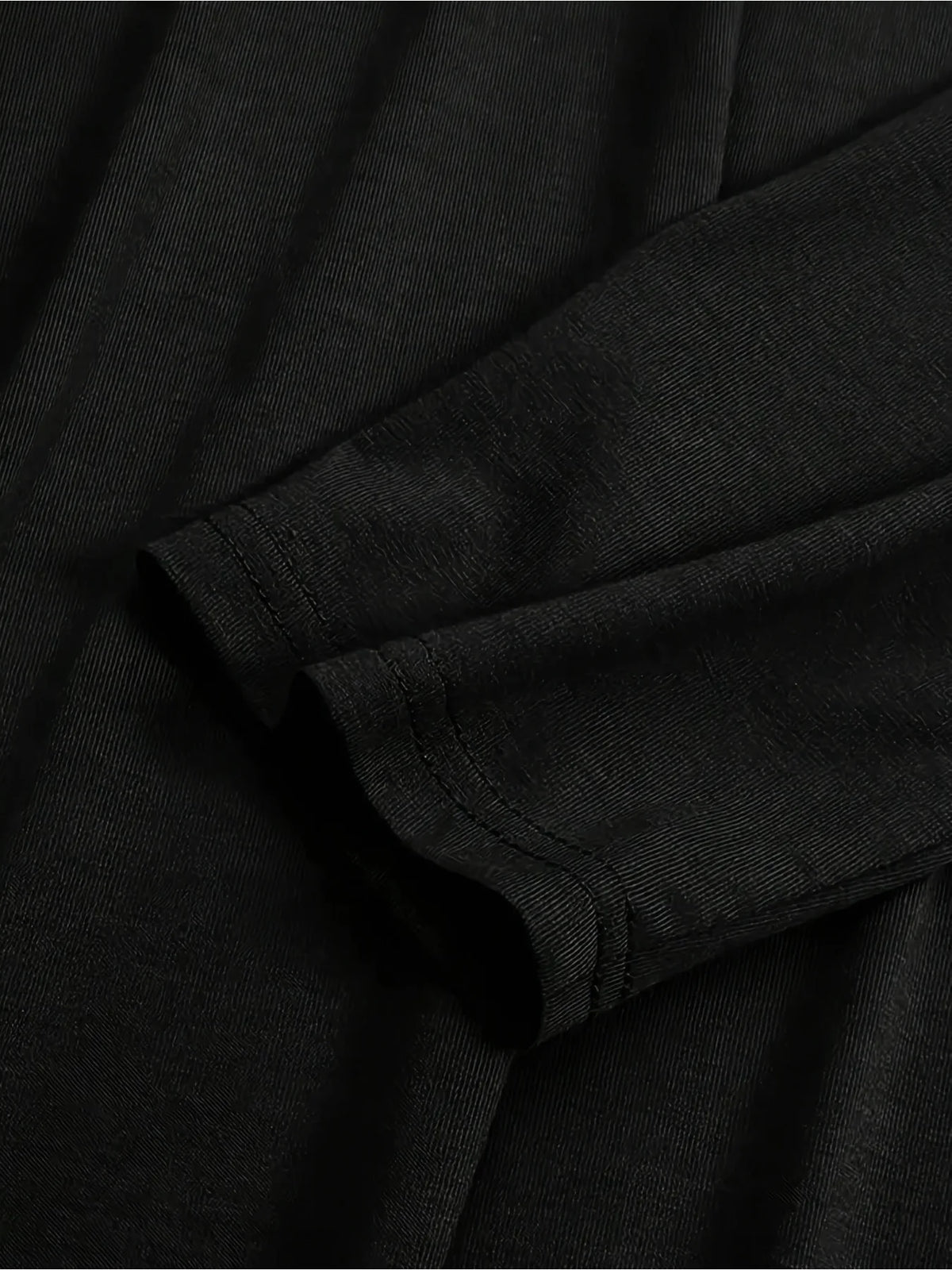 Gros plan sur la manche et le détail de tissu d'une robe longue ample noire.
