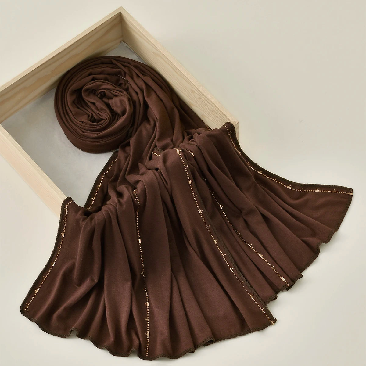 Pañuelo de jersey de algodón con brillo dorado marrón oscuro enmarcado en madera clara.