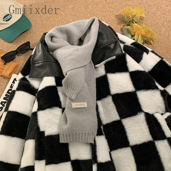 A gray knitted scarf is draped over a black leather jacket, which is part of a black and white faux fur plaid coat.
