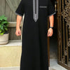 A man wearing a black Moroccan ethnic thobe with a stand collar and embroidered details.