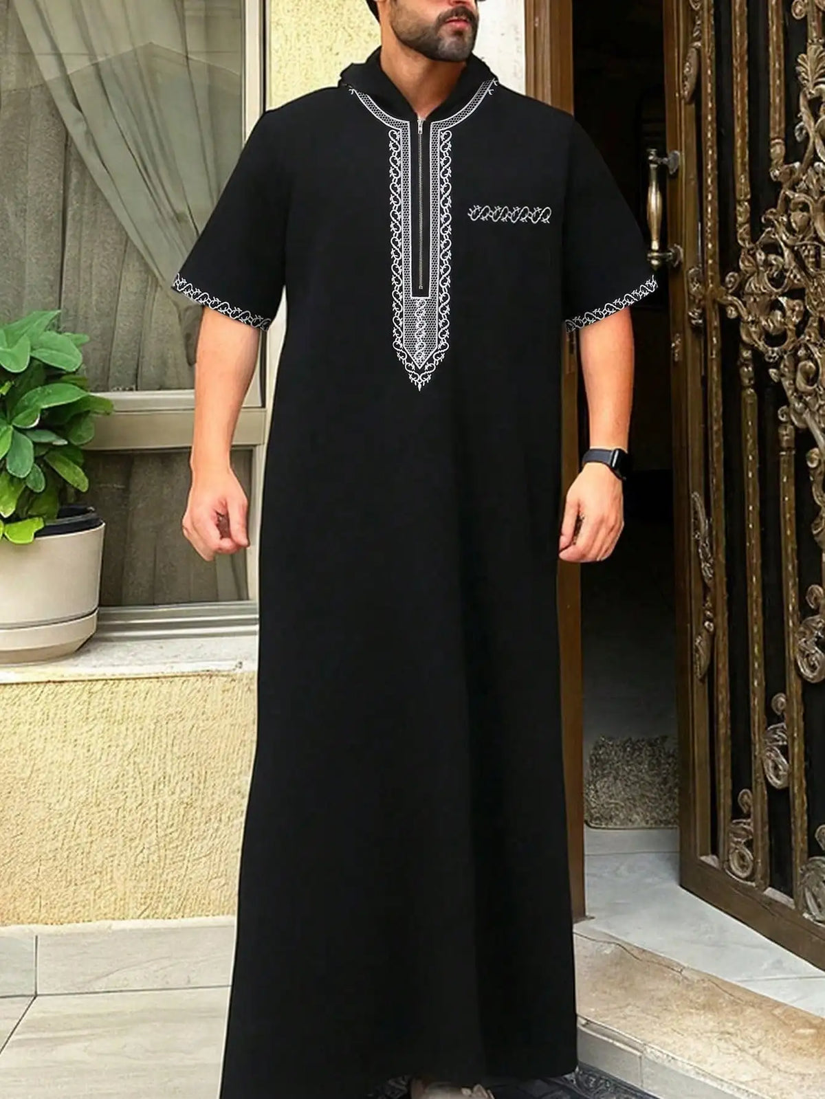 A man wearing a black Moroccan ethnic thobe with a stand collar and embroidered details.