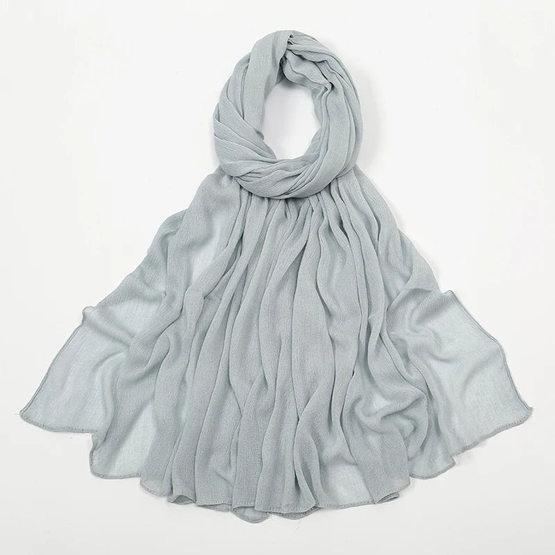 Écharpe châle en rayon gris clair, drapée autour du cou et flottant sur les épaules.