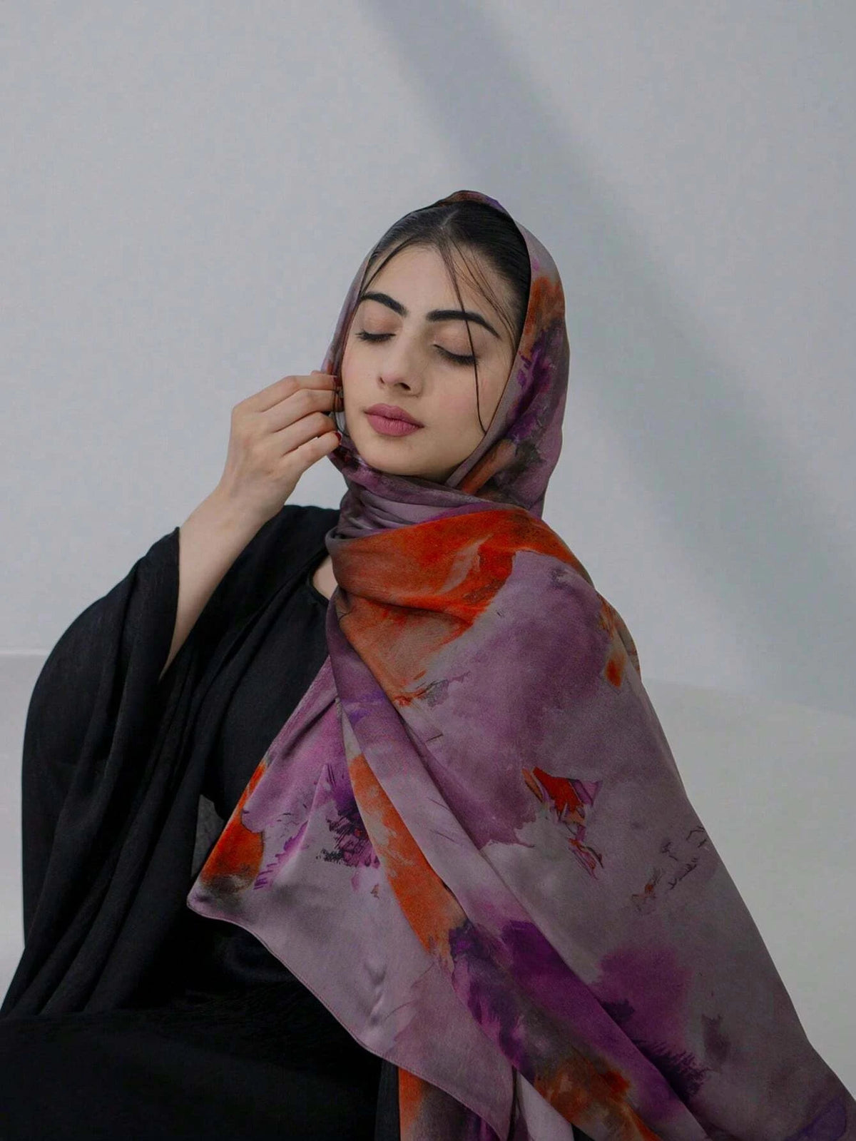 Eine Frau trägt einen lila-orangefarbenen Aquarell-Hijabschal über einem schwarzen Kleidungsstück.