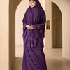 Eine Frau in einem eleganten, mehrlagigen Spitzen-Khimar-Abaya-Set in tiefem Violett steht in einem hellen, gewölbten Flur.
