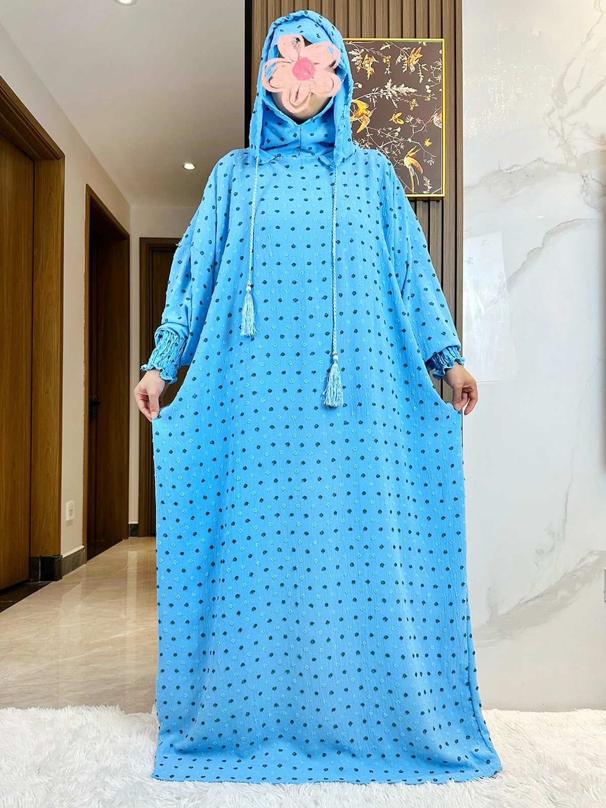 Una mujer vistiendo una abaya azul brillante de algodón con lunares negros y una cubrebocas floral rosa.