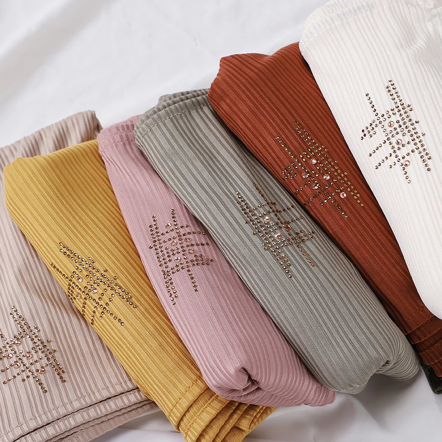 Eine Kollektion von gekräuselten Jersey-Hijab-Schals in verschiedenen Farbtönen wie Beige, Pink, Olivgrün und Rostbraun.