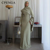 Eine Frau trägt ein elegantes, langärmeliges, olivgrünes, dehnbares Abaya-Kleid drinnen.