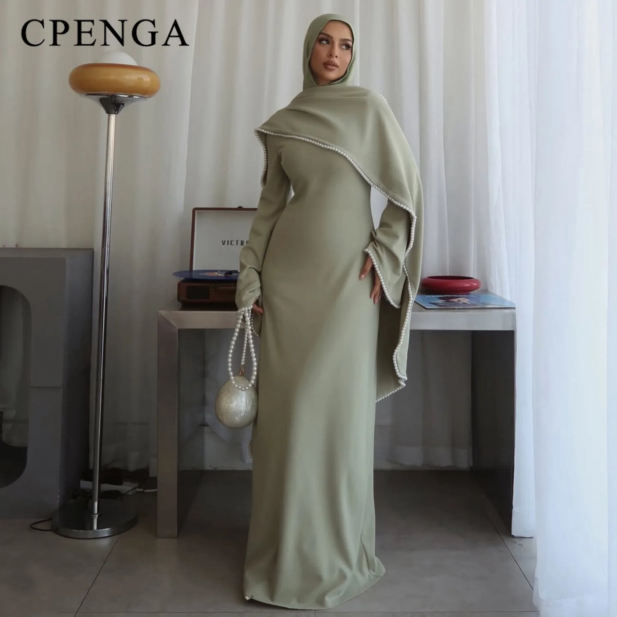 Eine Frau trägt ein elegantes, langärmeliges, olivgrünes, dehnbares Abaya-Kleid drinnen.