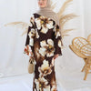 Eine Frau in einem braun-cremefarbenen floralen Abaya mit Hijab vor weißem Hintergrund.