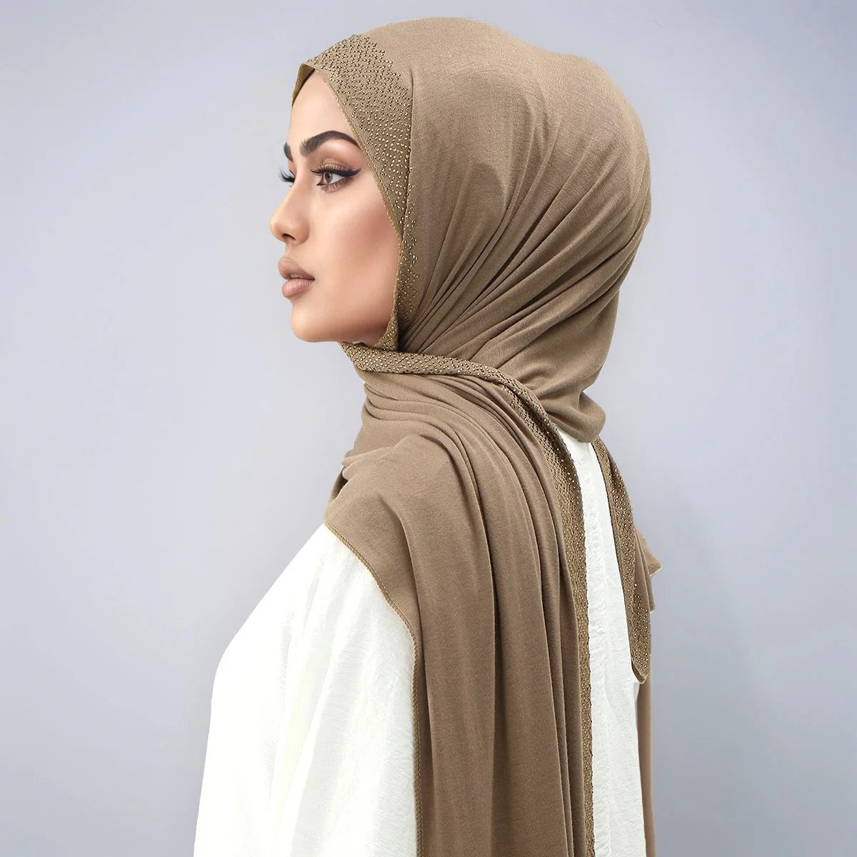 Eine Frau trägt einen beige schimmernden Strass-Seidenschal als Hijab über Kopf und Hals.