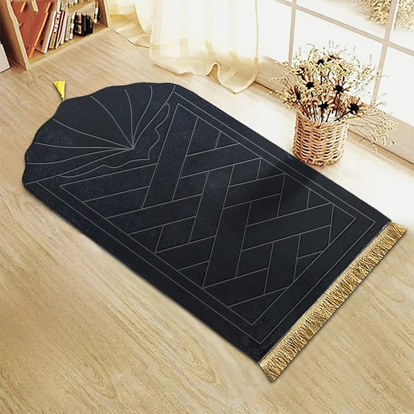 A black prayer mat with an embossed geometric pattern and gold decorative tassels placed on a light wooden floor.