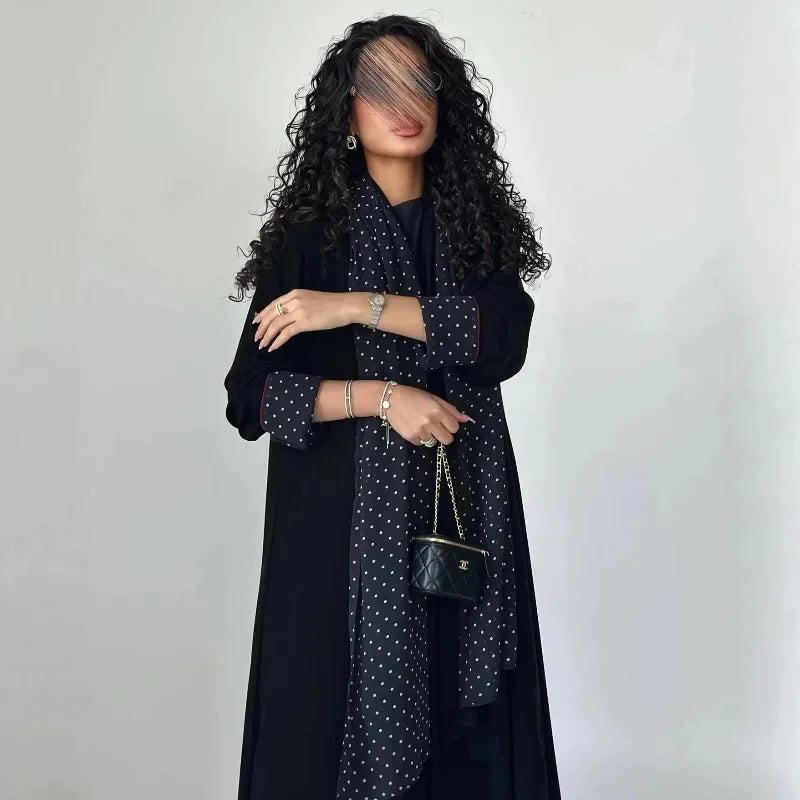 Eine Frau trägt ein elegantes schwarzes Abaya-Cardigan-Kleid mit Polka-Dot-Muster und ein langes schwarzes Oberteil.
