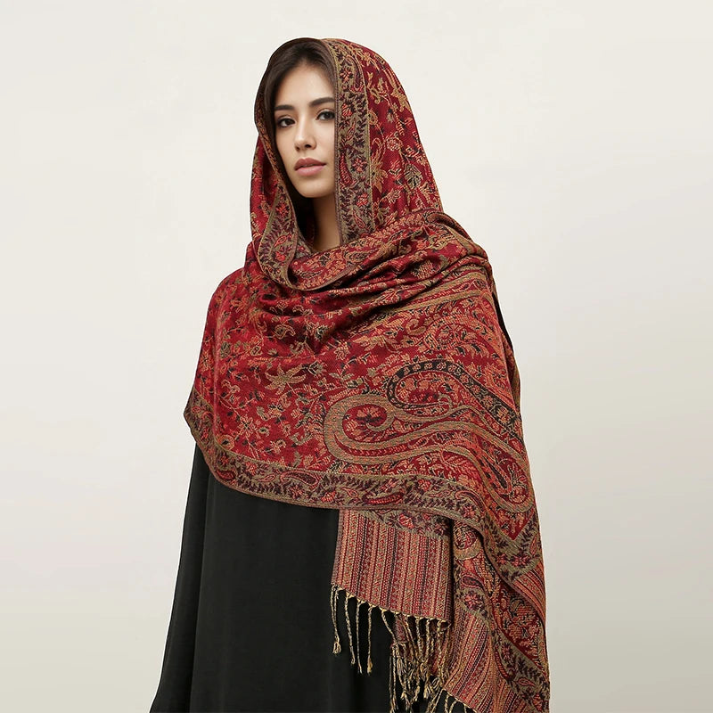 Una mujer usando un pañuelo pashmina de lujo estampado en rojo y oro sobre su cabeza y hombros.