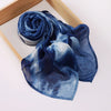 Un foulard voile imprimé bleu indigo profond roulé et drapé sur un plateau en bois.