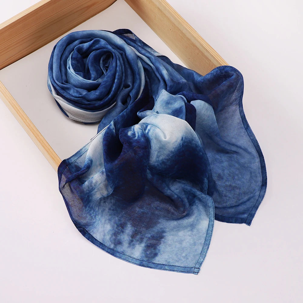 Un foulard voile imprimé bleu indigo profond roulé et drapé sur un plateau en bois.